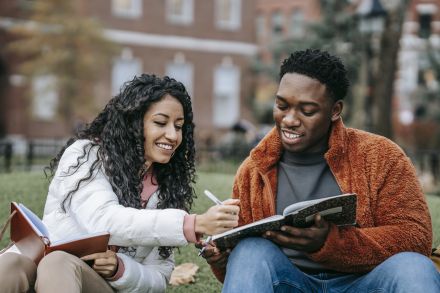 Man and Woman Holding Notebooks While Sitting on Grass